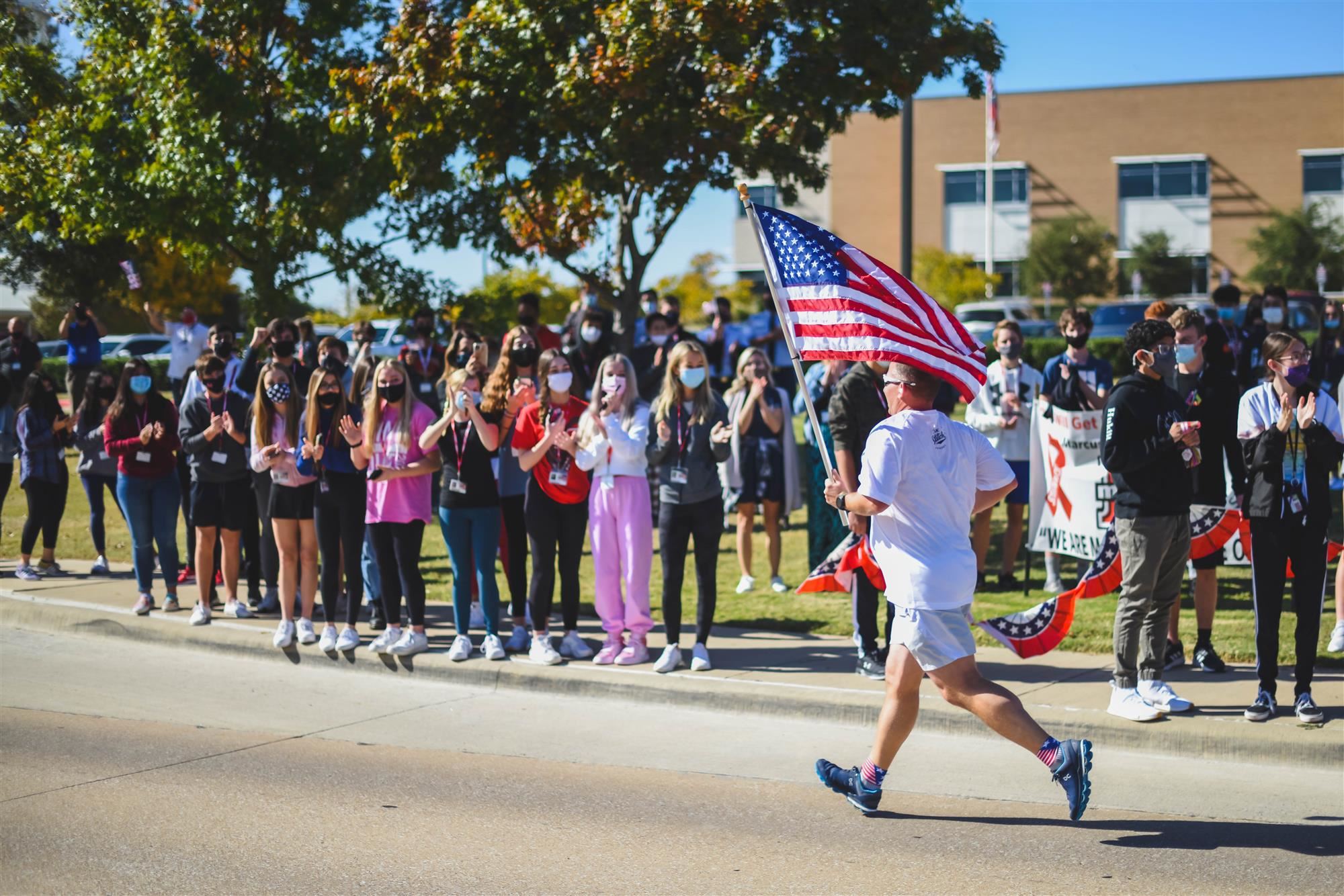 Man runs with flag as students cheer along. 