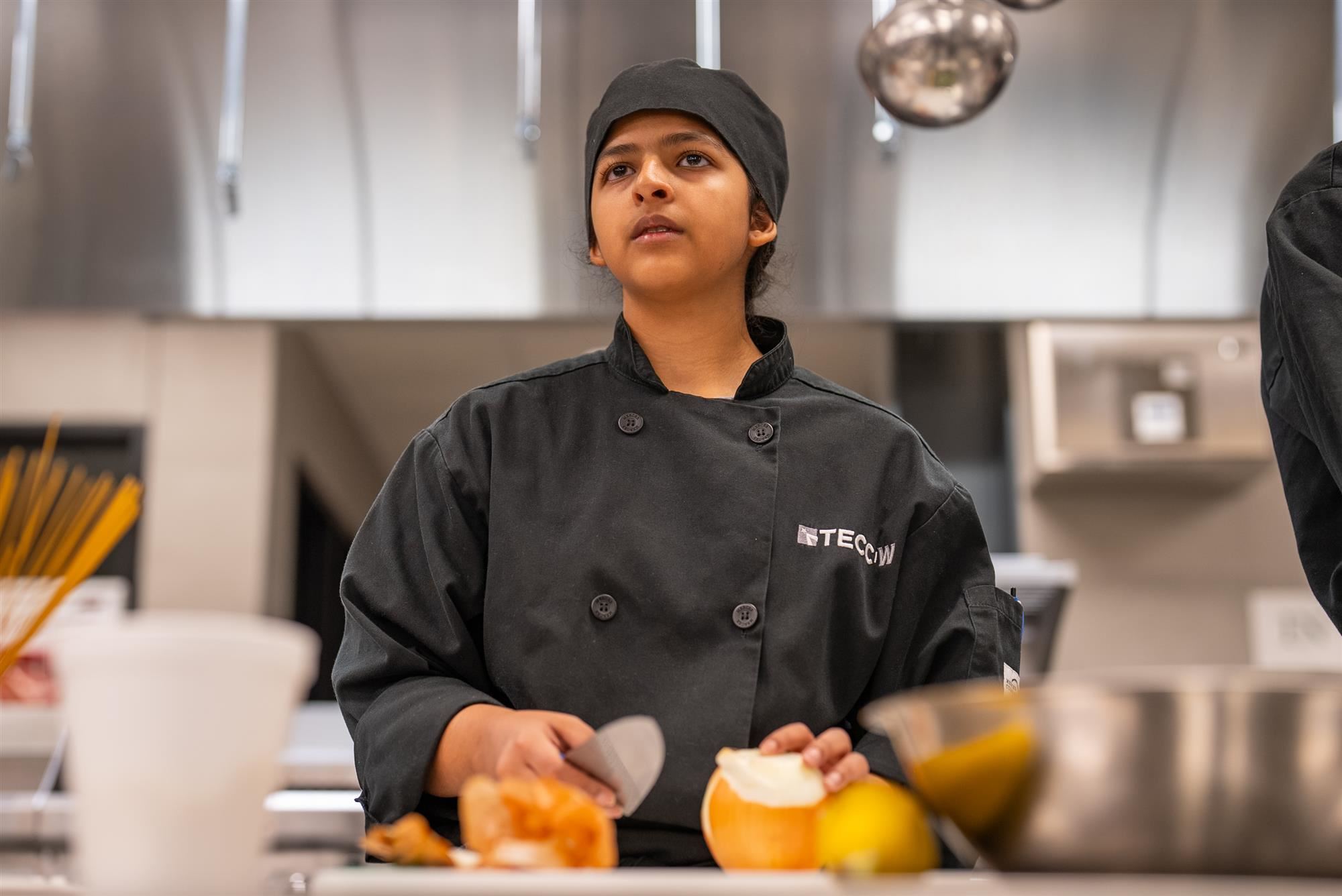 A TECC-West Culinary students chops an onion at her prep station