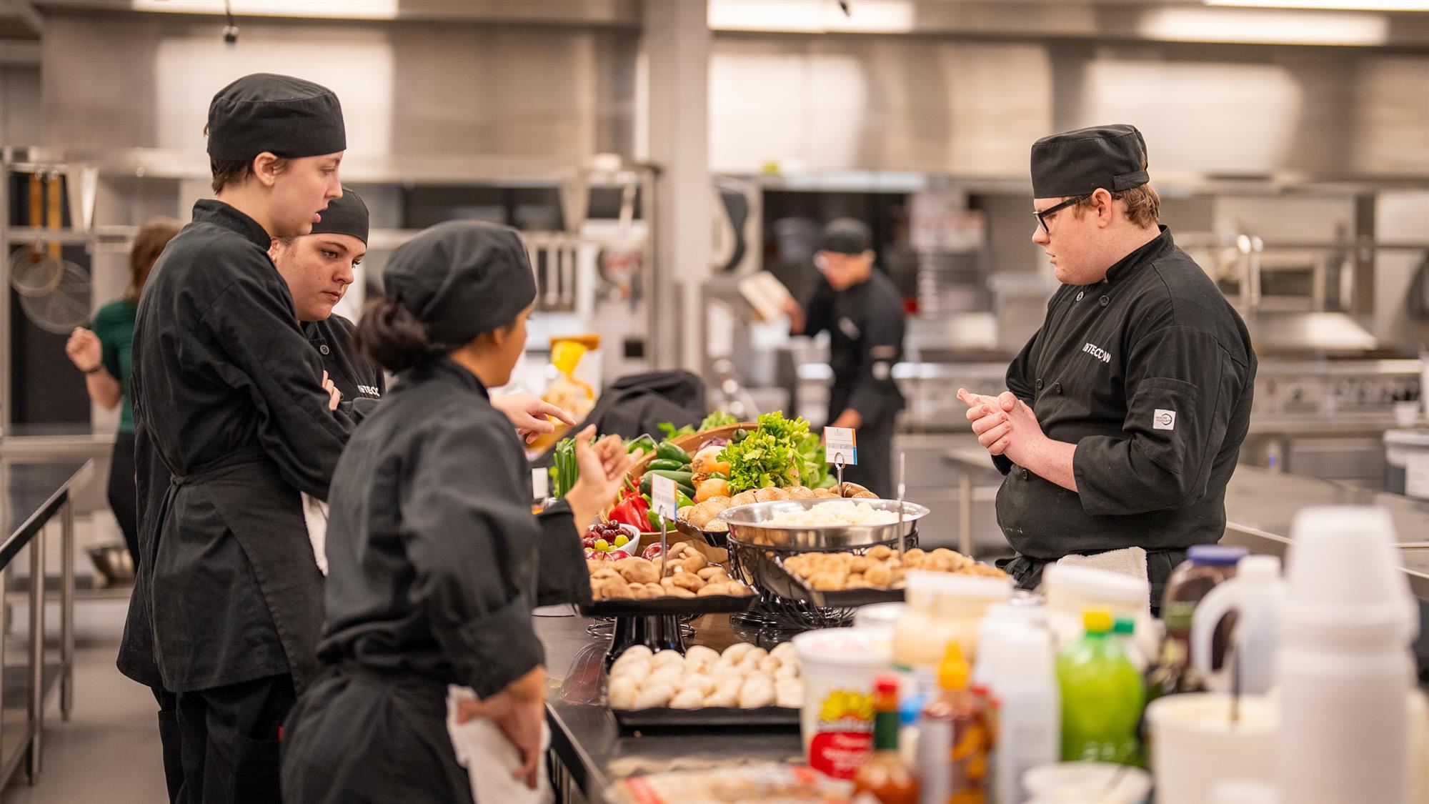 TECC-West Culinary students discuss recipes over a table full of ingredients
