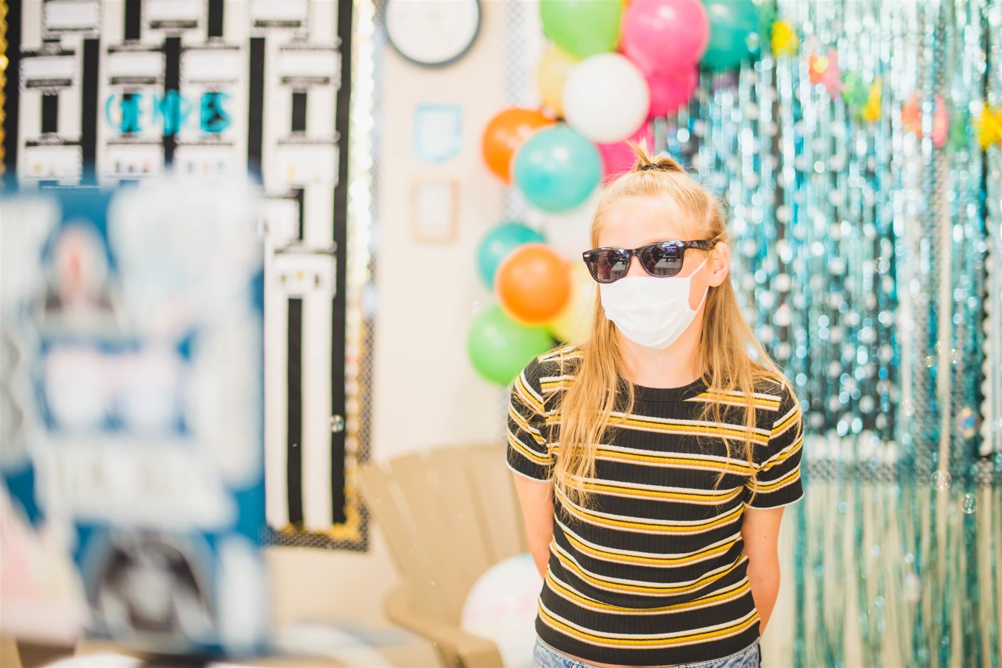 Student in sunglasses and mask looks towards laptop screen 