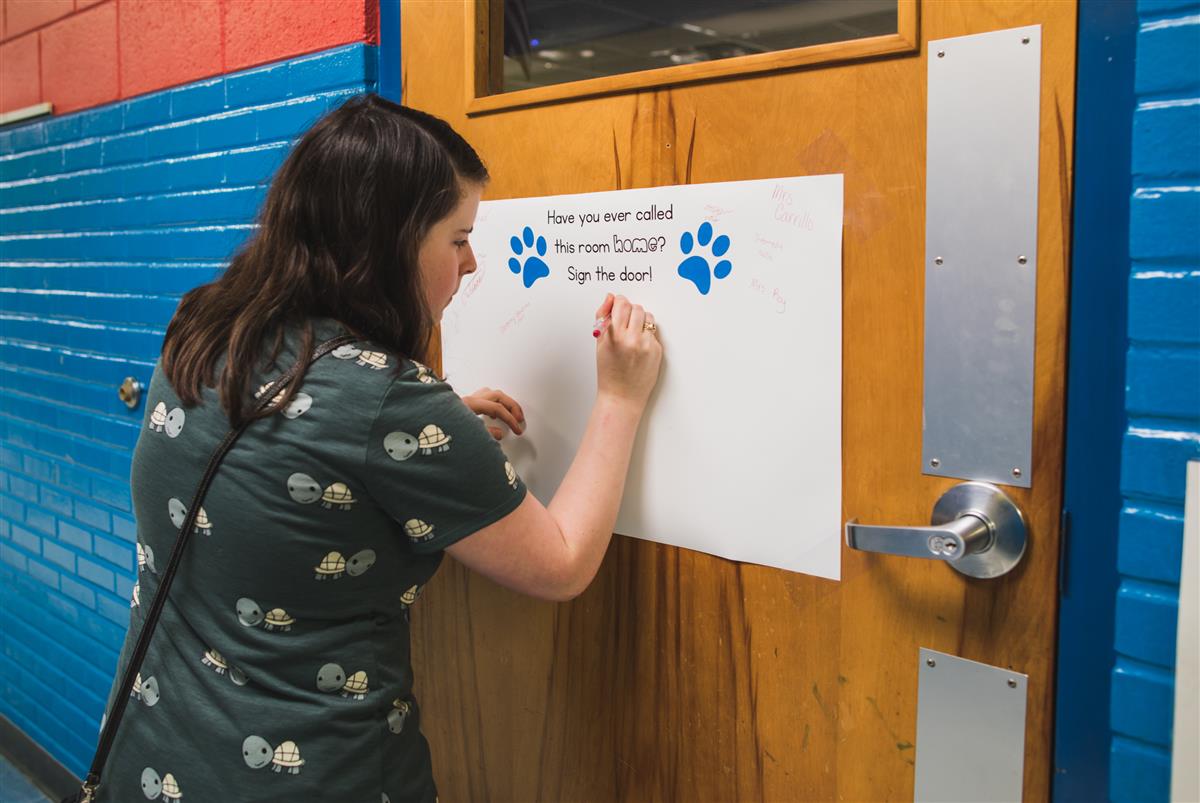 Former student signs poster on old classroom door. 