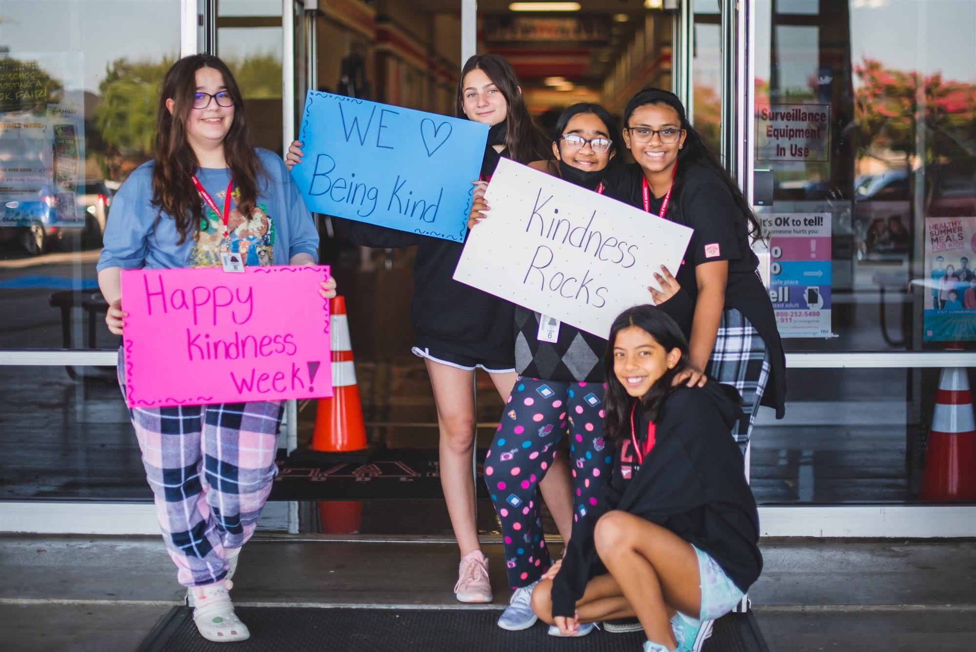 Students in pajamas hold greeting signs at school front door