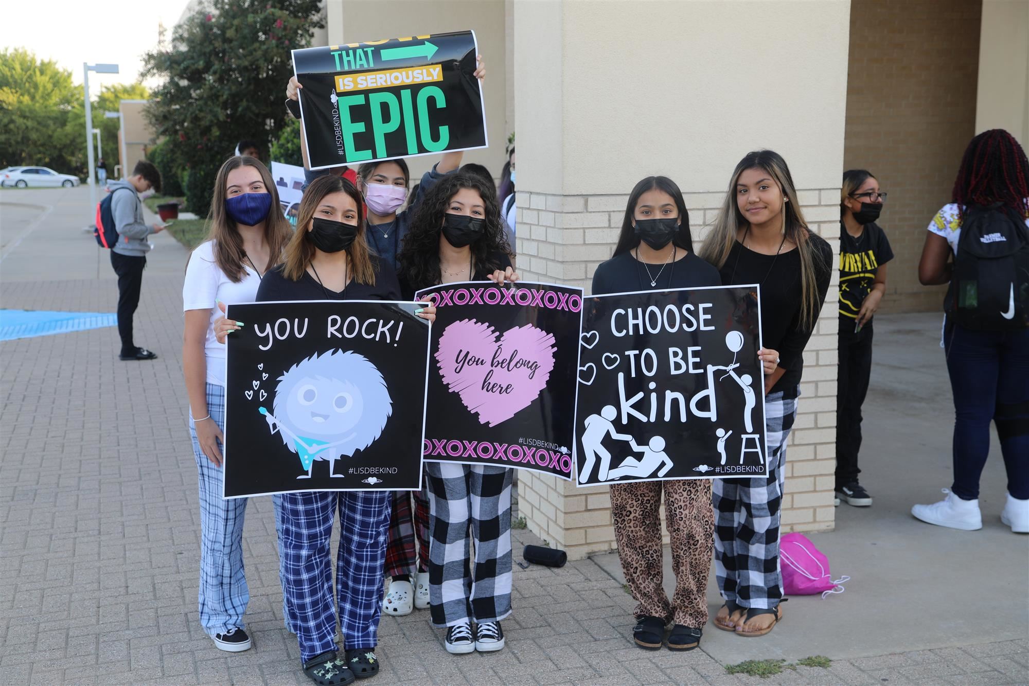 Students in pajamas hold greeting signs outside school