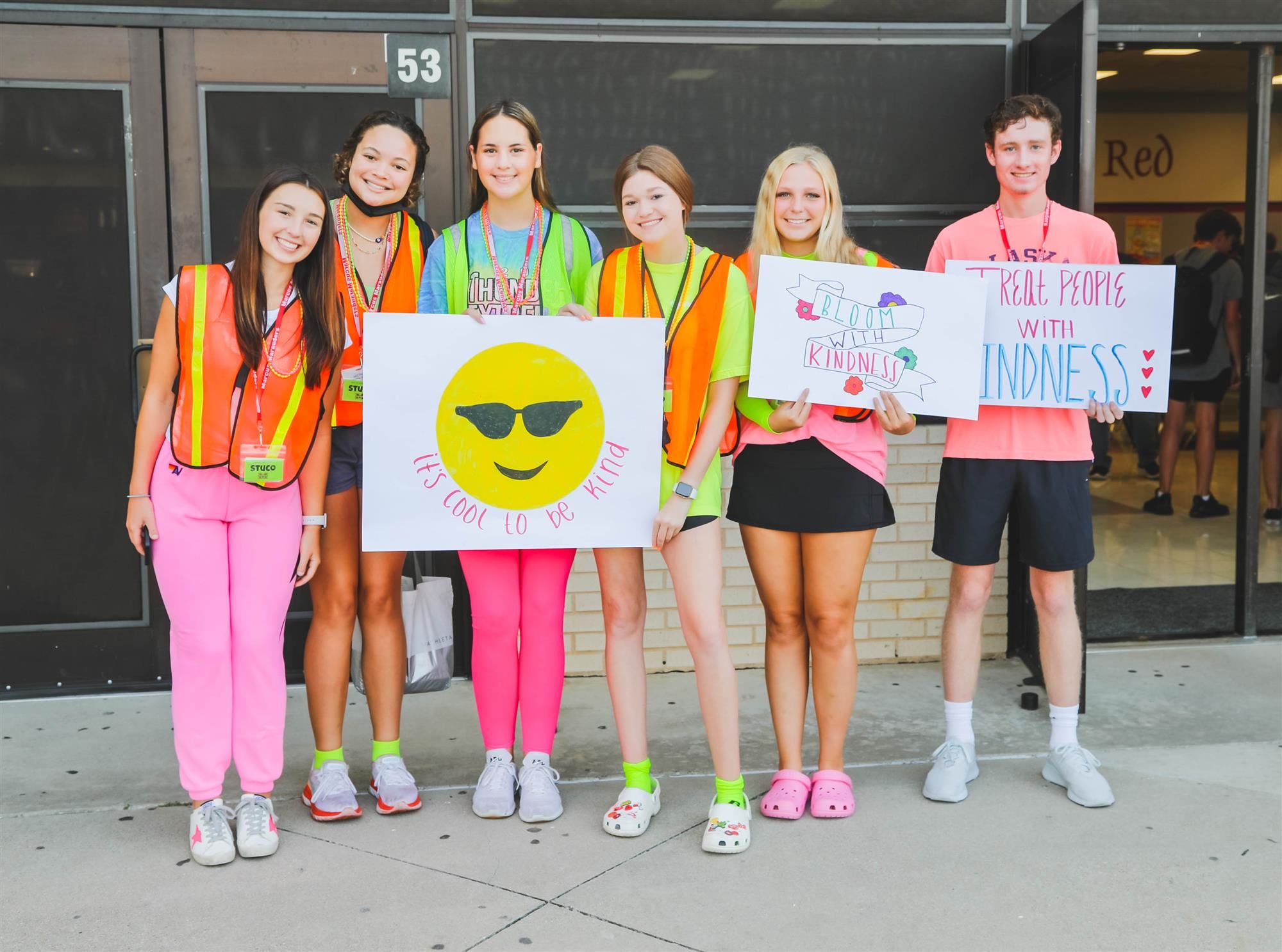 Students in neon stand at school door with signs