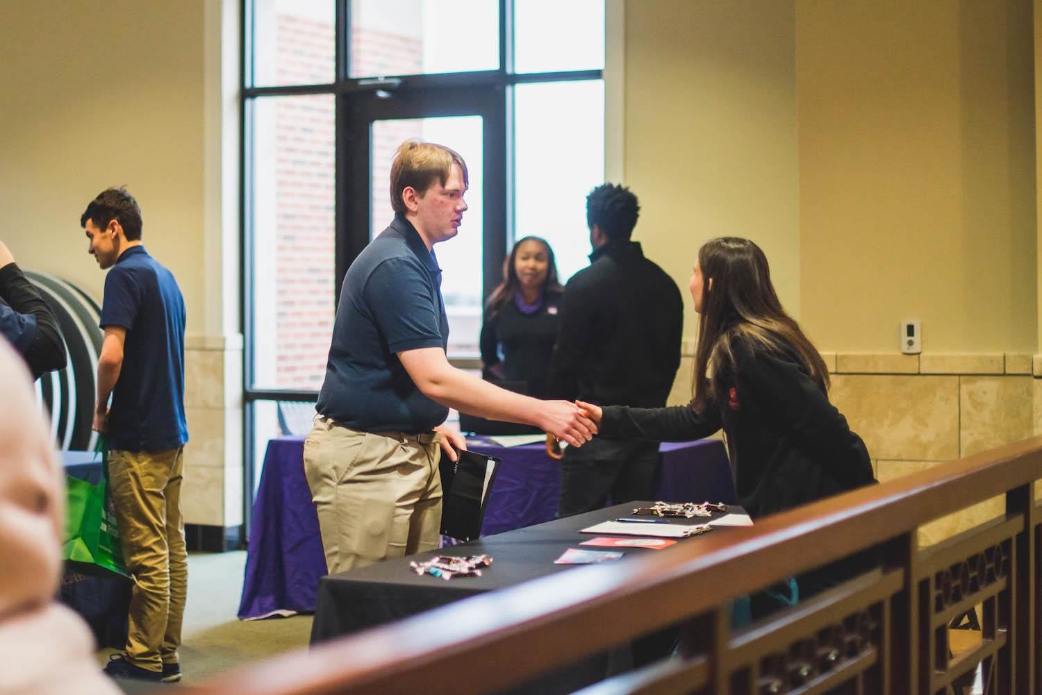 student shakes hands with potential employer at job fair 