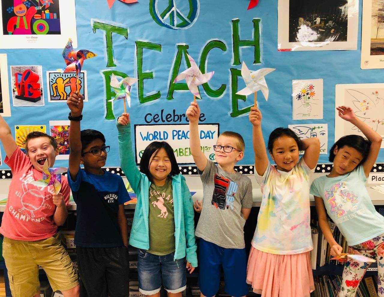 Bluebonnet students hold up their pinwheels in front of teach peace sign in the school. 2019 