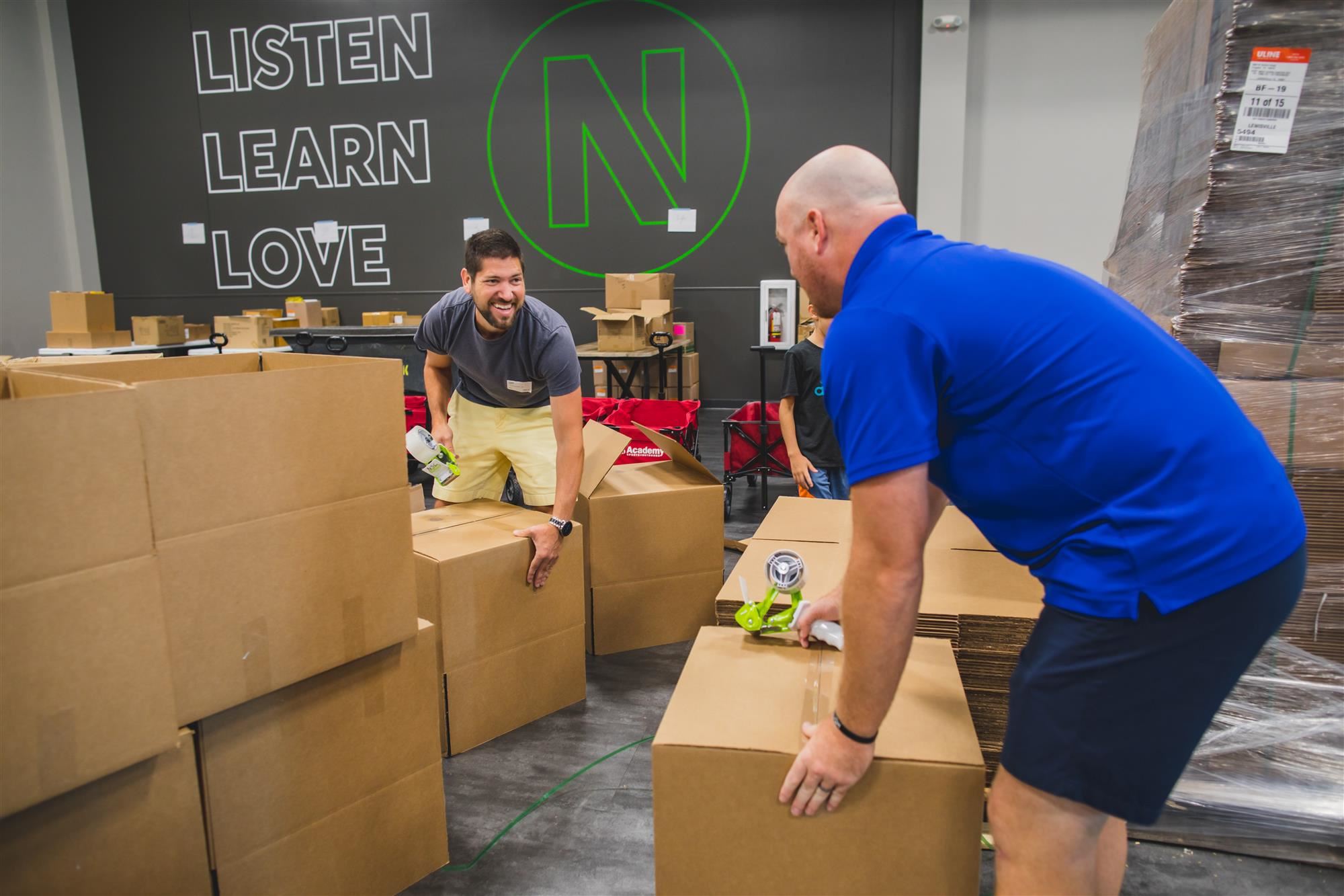 Volunteers pack stuffed backpacks into boxes for future campus delivery.